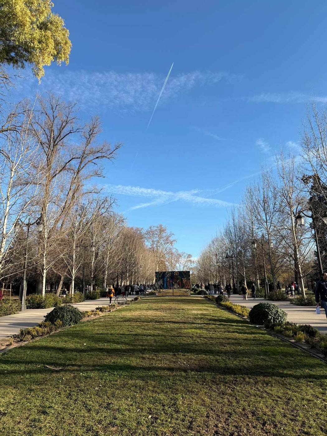 Niños y adultos caminando por un parque madrileño, escena espontánea, luz de tarde.