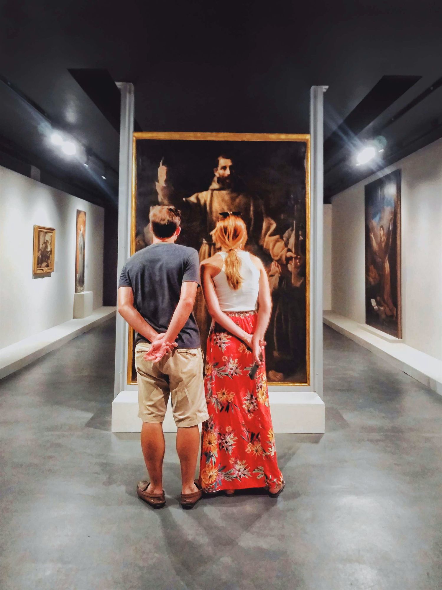 Interior de museo o galería, figura humana de espaldas observando una obra, luz suave.
