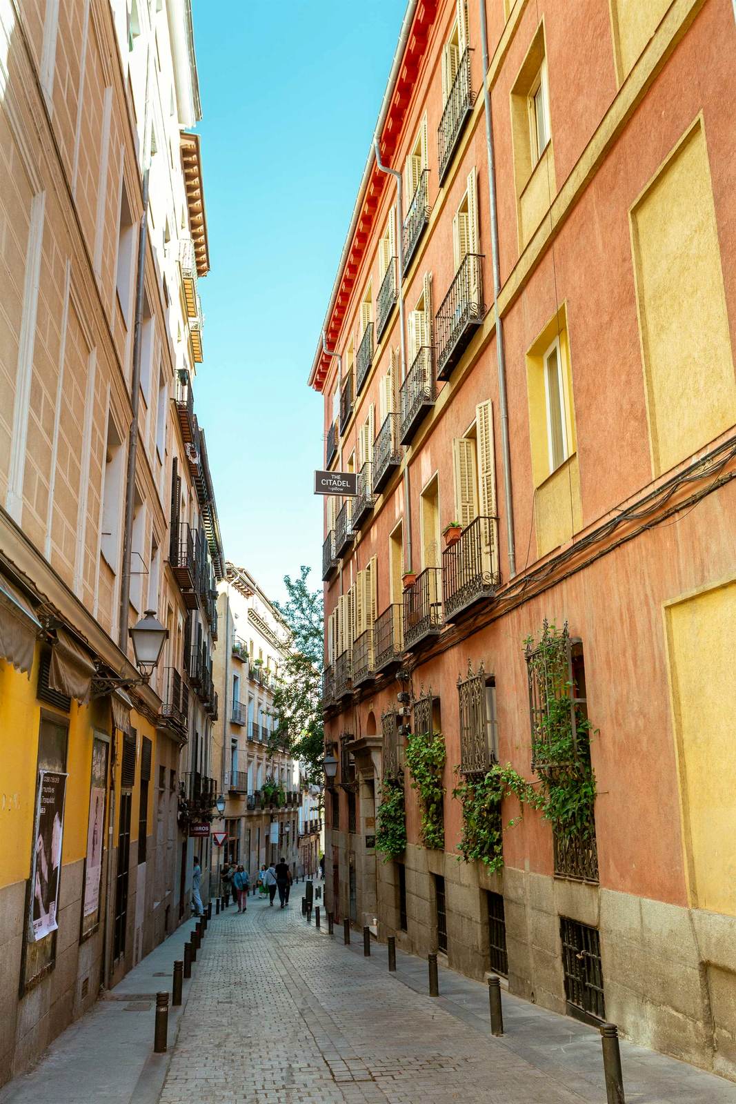 Calle residencial de Chamberí por la mañana, balcones con rejas de hierro, toldos, movimiento discreto de vecinos.